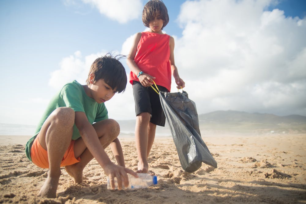 Two boys picking up a plastic bottle on a sand beach